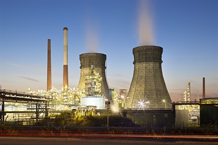 An oil refinery with two cooling towers and blue night sky.
