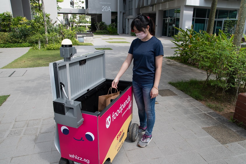 A woman retrieving a food delivery bag from a FoodBot