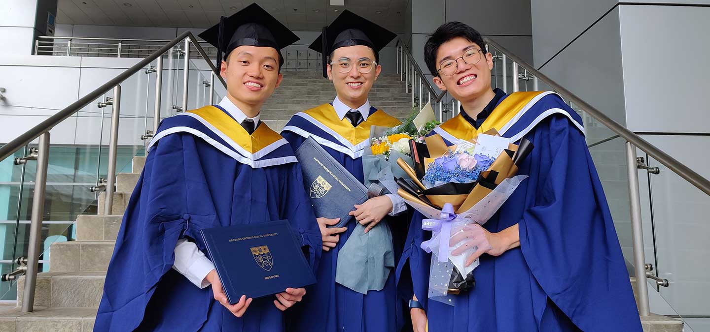 A group photo of 3 undergraduates in convocation gown holding graduation certificates and bouquet of flowers.