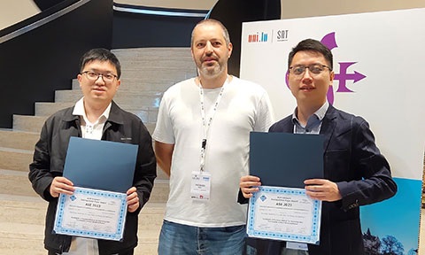 Thumbnail photo of 2 researchers holding cert standing between a presenter.