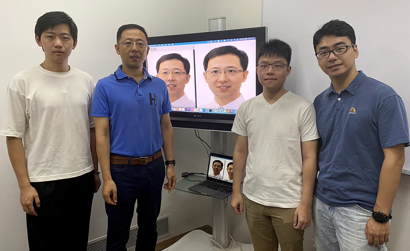 Photo of researchers standing beside a digital display screen with their project featured.