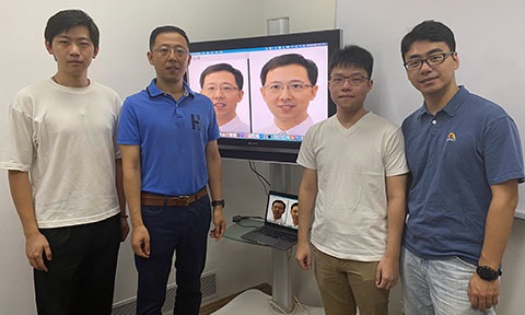 Photo of researchers standing beside a digital display screen with their project featured.
