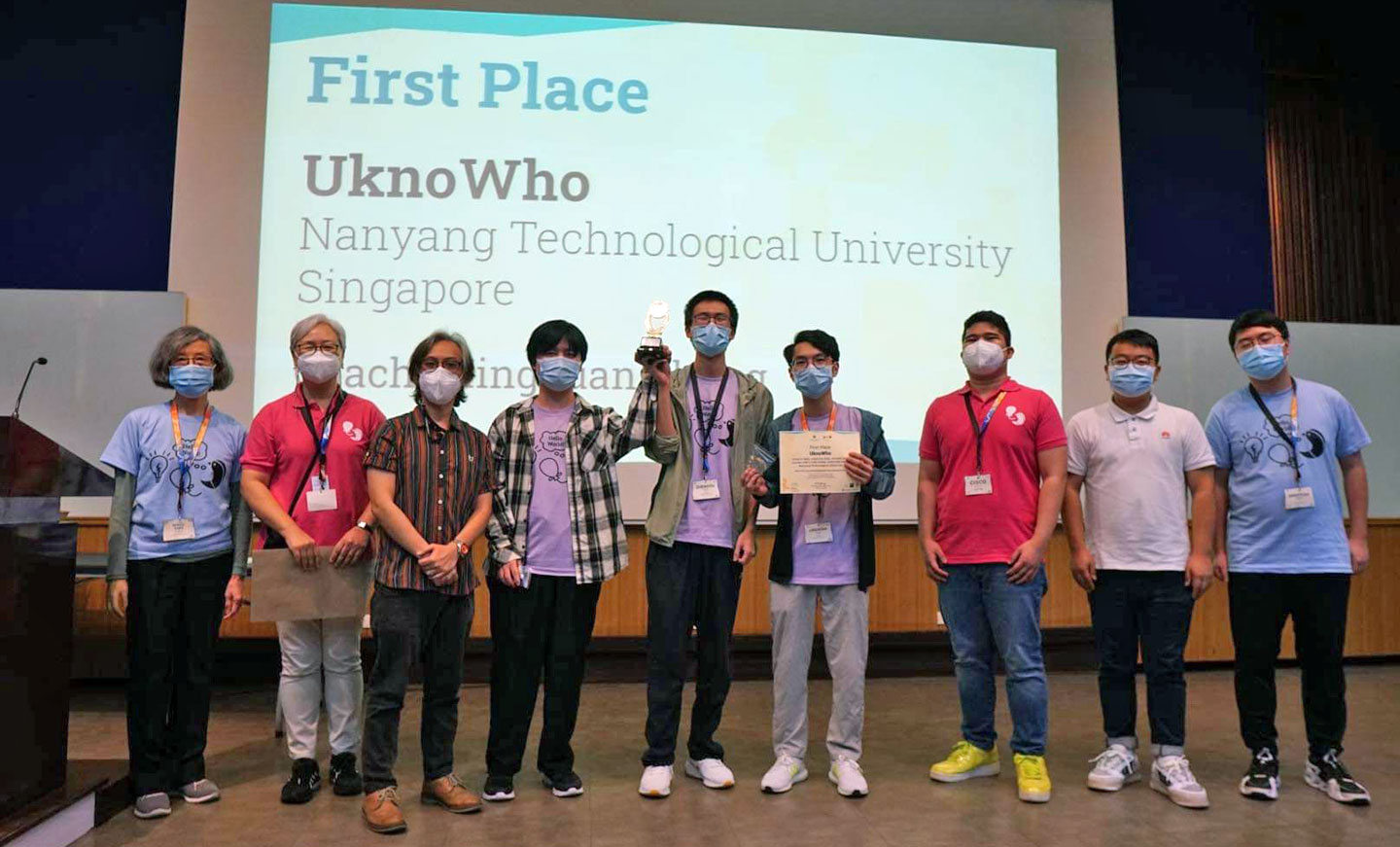 Photo of university students holding a trophy and certificate on stage.
