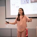 Female speaker dressed in pink, shares her entrepreneurial journey confidently during a campus forum.