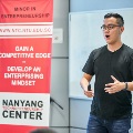 Male speaker, Karl Mak, dressed in a black top, speaks confidently at an event