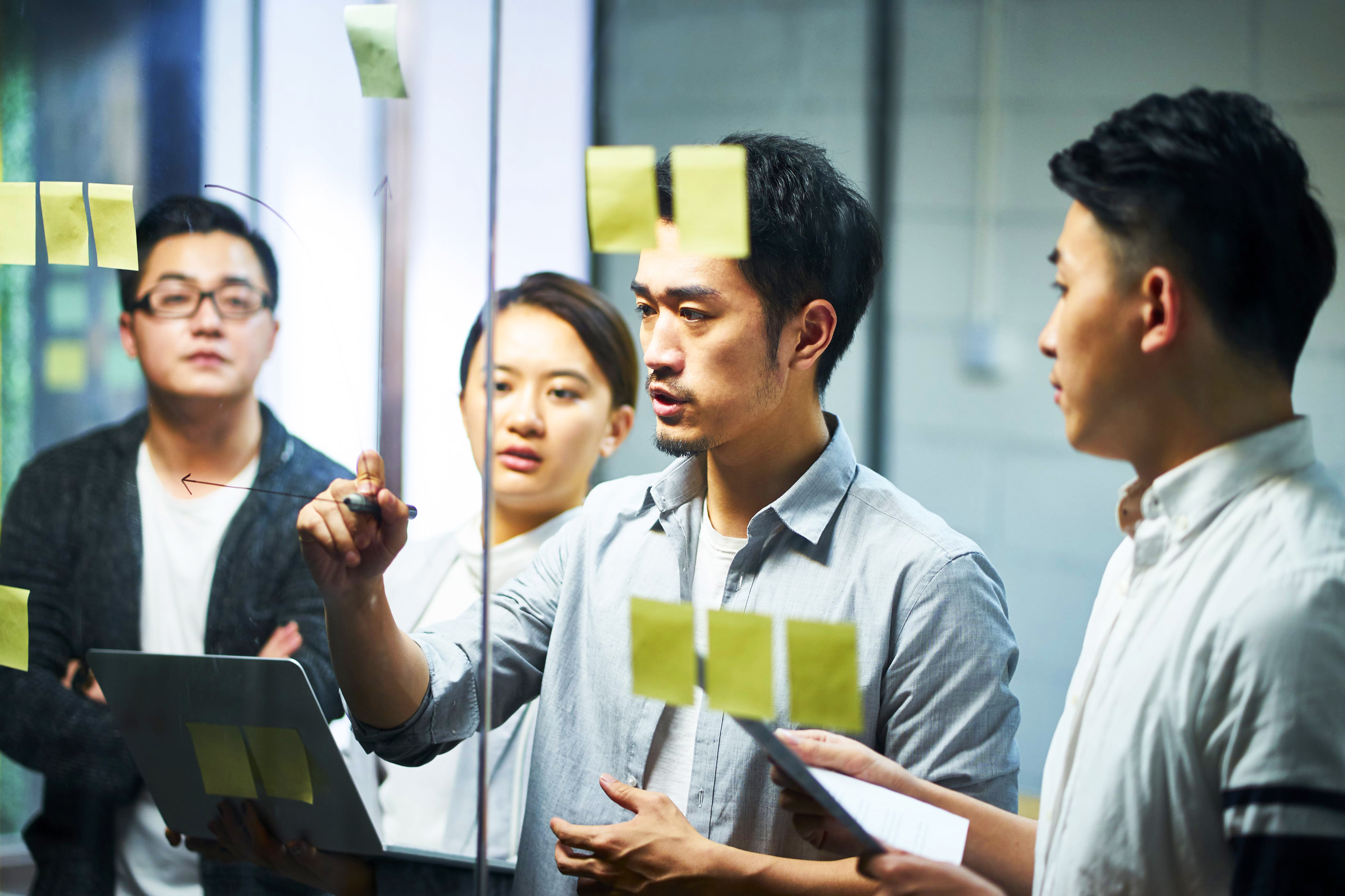 Male student drawing conclusions, linking ideas and writing solutions on a glass board