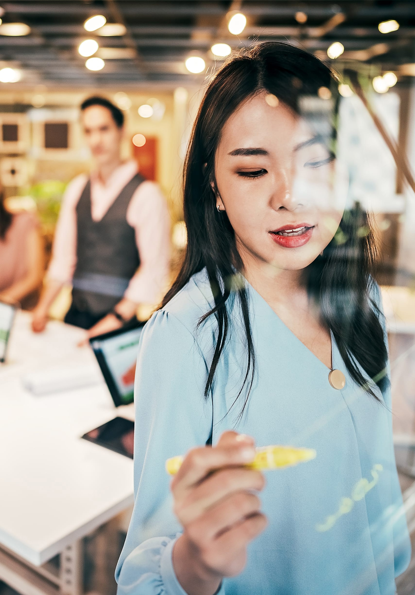 Female student writing on a glass board with yellow marker
