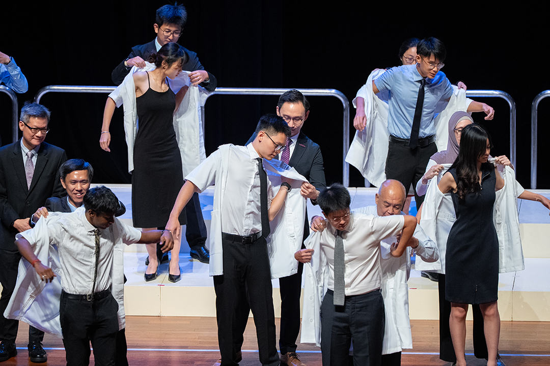 Student dons white coat with the help of prof