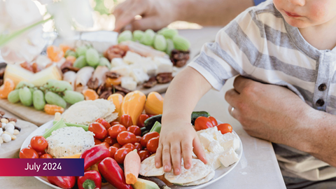 A child placing his hand on a plate full of vegetables with July 2024 text on bottom left
