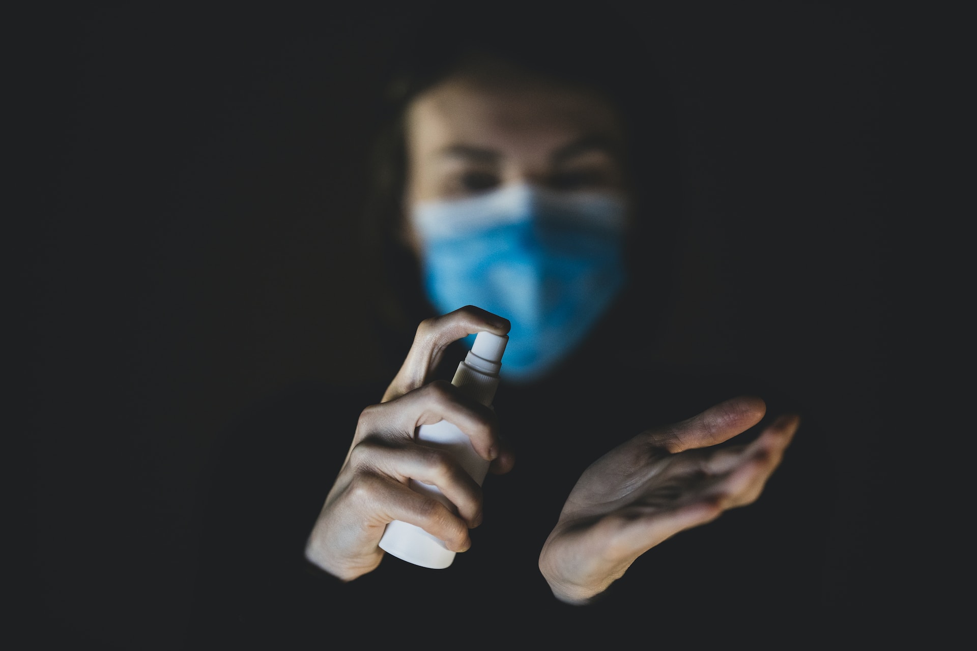 A man wearing a surgical mask using a hand sanitizer