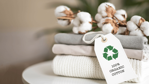 Close-up of cotton placed on folded apparel with a tag featuring a recycling icon and the text '100% organic cotton'