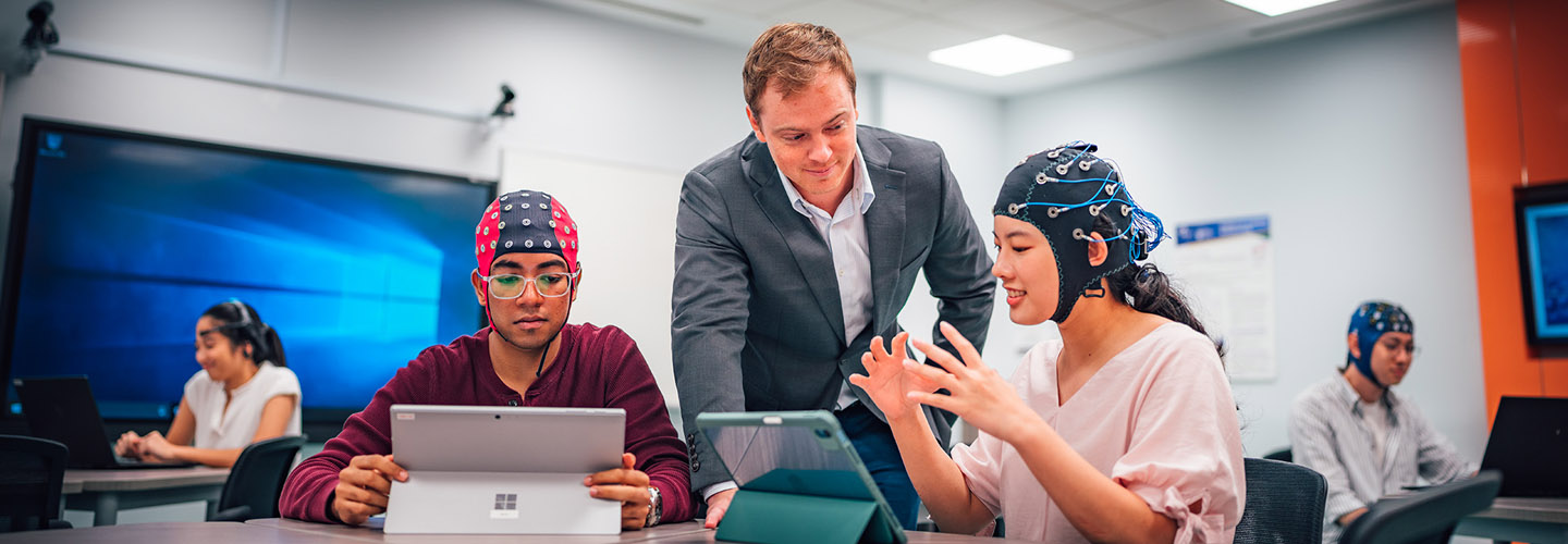 2 Students Wearing A Brain Scan Cap And A Caucasian Teacher In Grey Suit