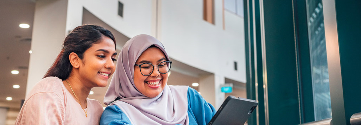 Malay Student Wearing Tudung with Indian Girl in Pink Top Looking at iPad in NIE Library