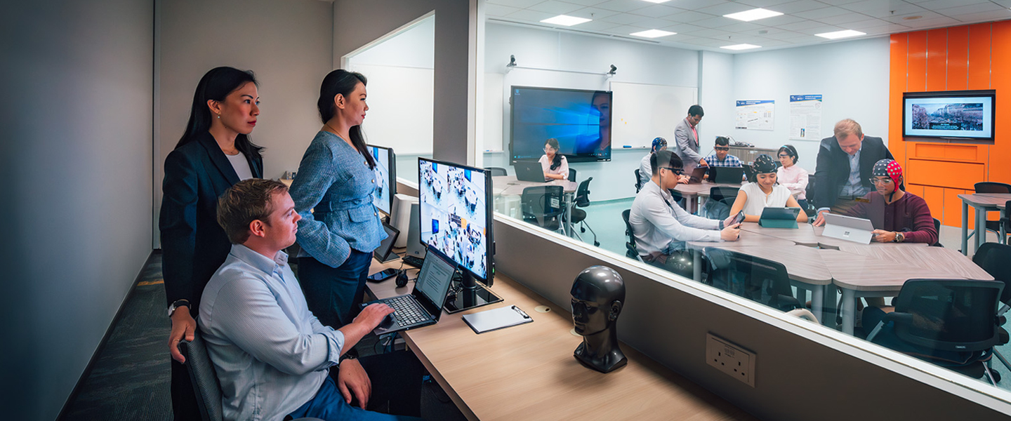 SoLEC Classroom with Caucasian Man Looking At Computer Screen Monitoring Students On The Inside Of Classroom Behind The Glass Window