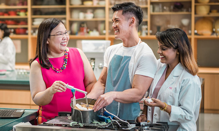 Experiment With A Pot Over A Stove Female Teacher In Bright Pink Top And 2 Students In Science Lab  (720x432px)