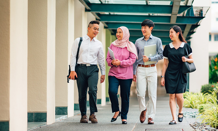 Walking Group of 4 Young Adults Chinese Boy in White Shirt Malay Girl in Pink Tudung Along Campus Corridor Next to Trees (720x432px)