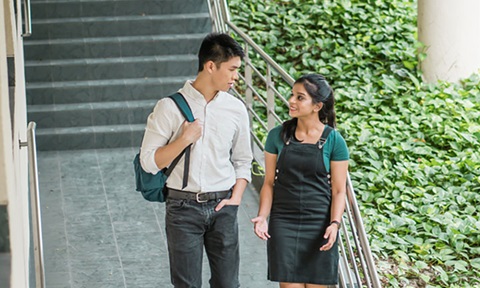 Walking Shot Chinese Boy with Backpack and Indian Girl in Dungaree Dress Talking at Staircase (720x432px)