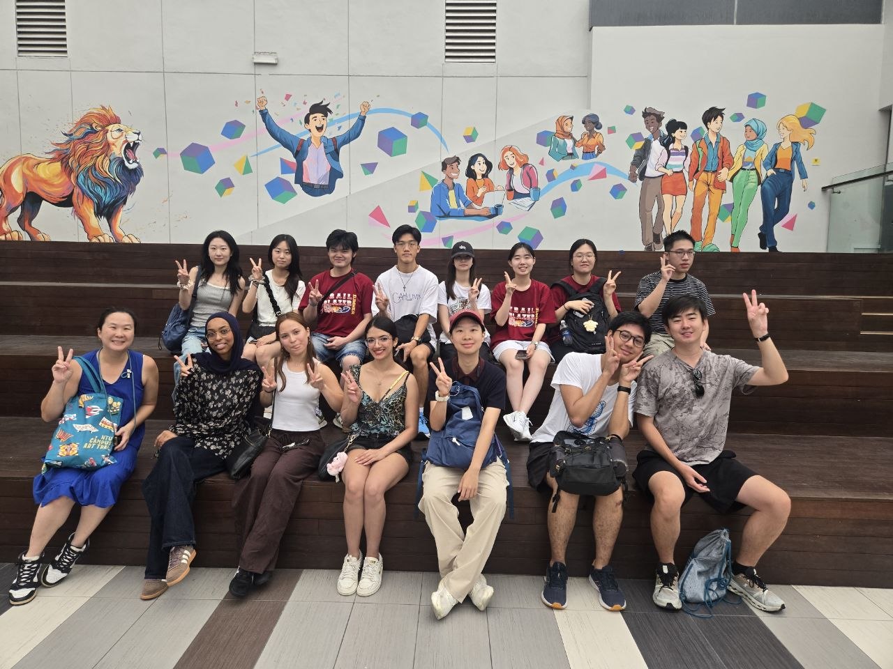 cat-walk-gem-summer-2025-group-onentu Group photo of people sitting on wooden steps in two rows in front of a colourful mural featuring a lion, happy people and graphic shapes