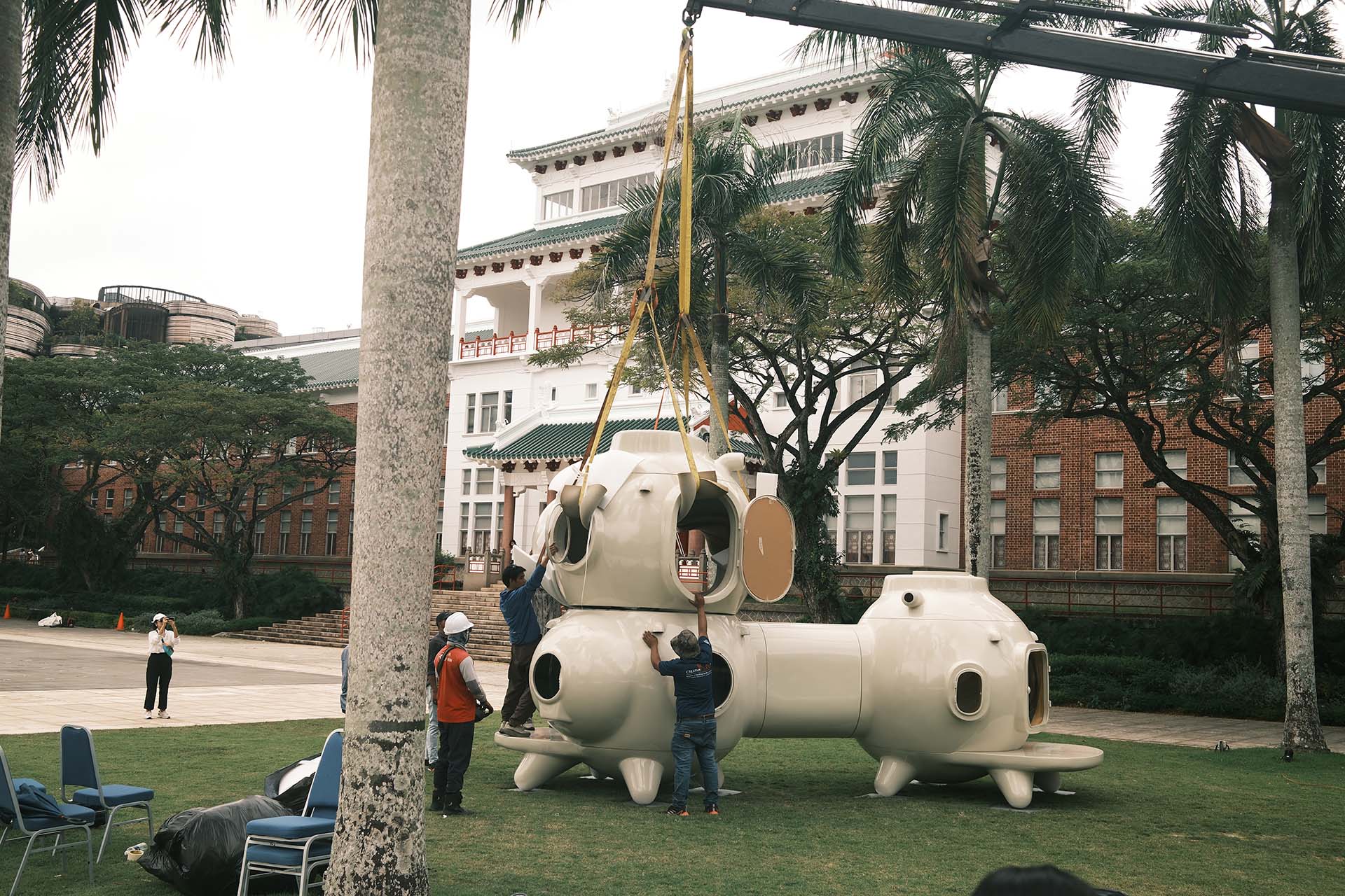 Crane moving a large white structure on a lawn