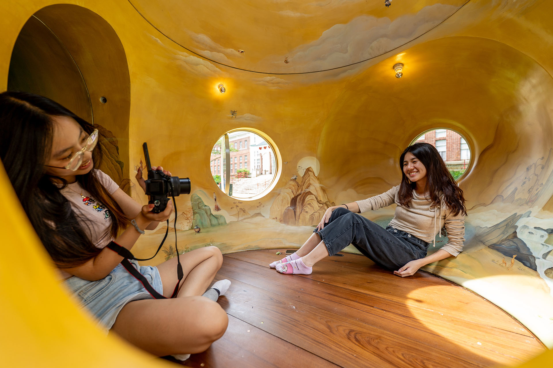 Two girls taking a photo in a structure with yellow painted walls