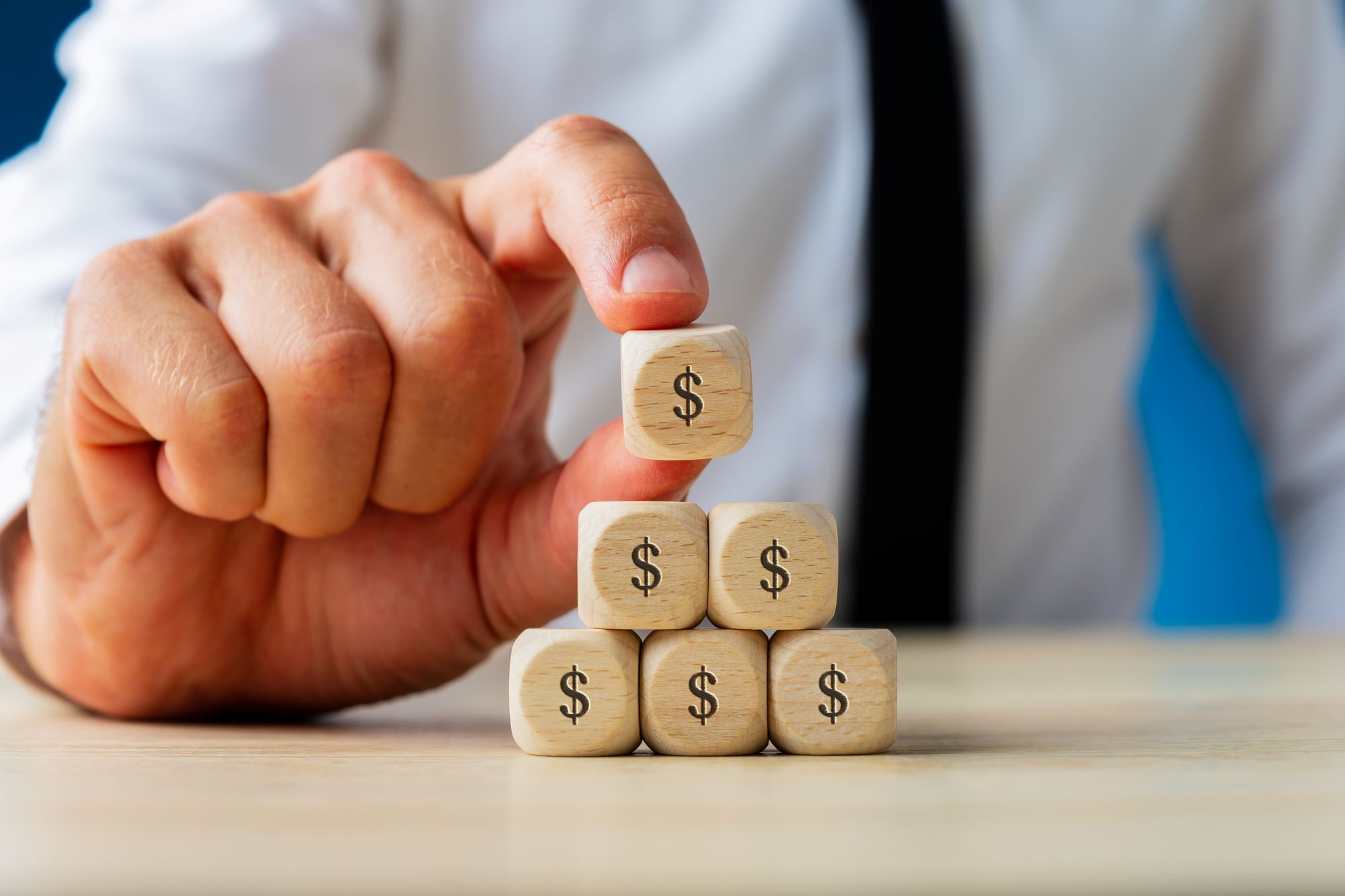 businessman making pyramid shape of wooden dices with dollar sign on them