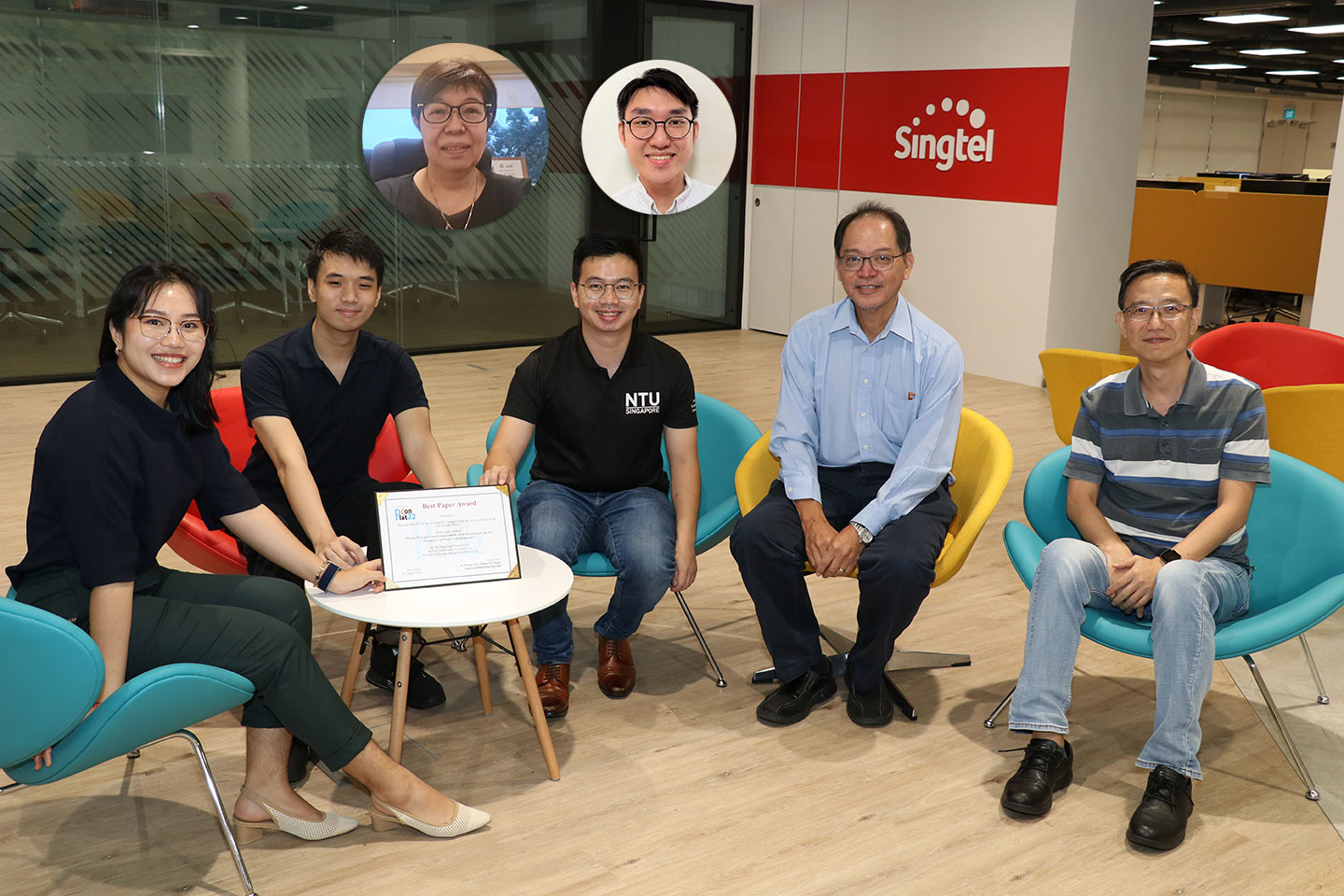 Photo of a group of researchers and students sitting infront of a small coffee table with a certificate on it.