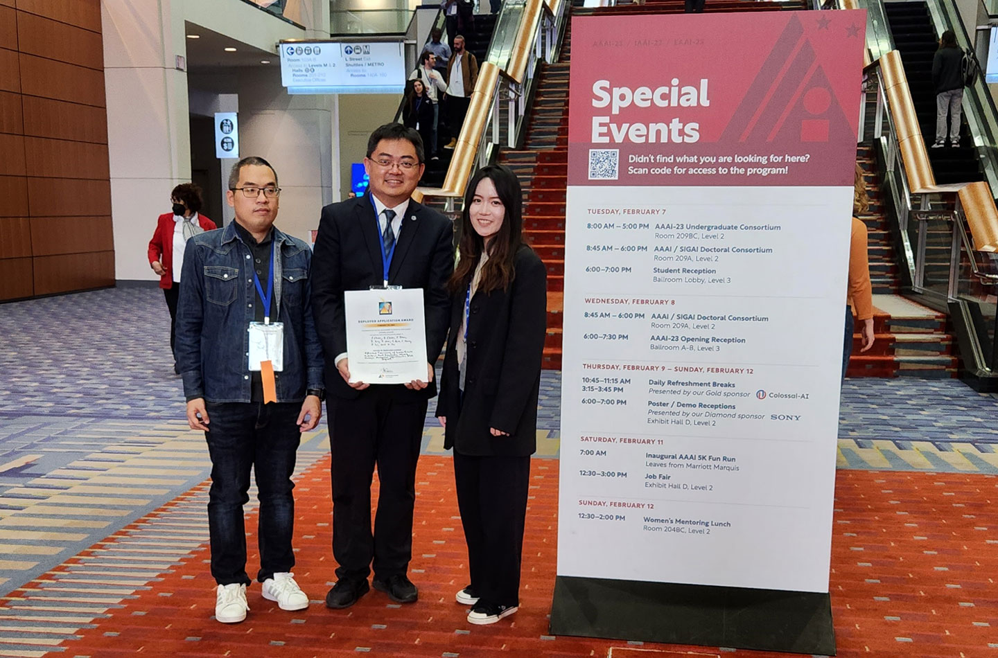 Photo of a professor holding an award certificate standing between 2 postgrad students, 1 male and 1 female..