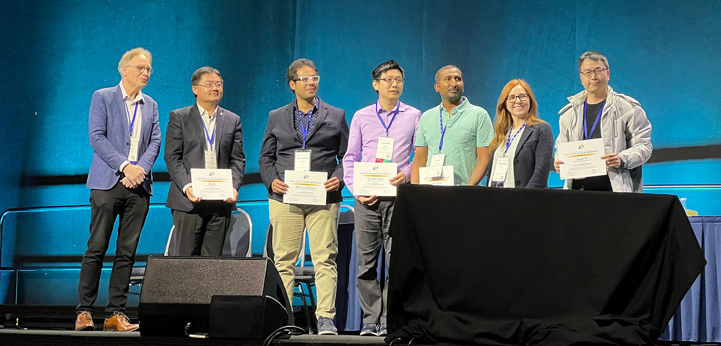 Photo of a presenter and a group of 6 awardees holding their awarded certificate on stage.