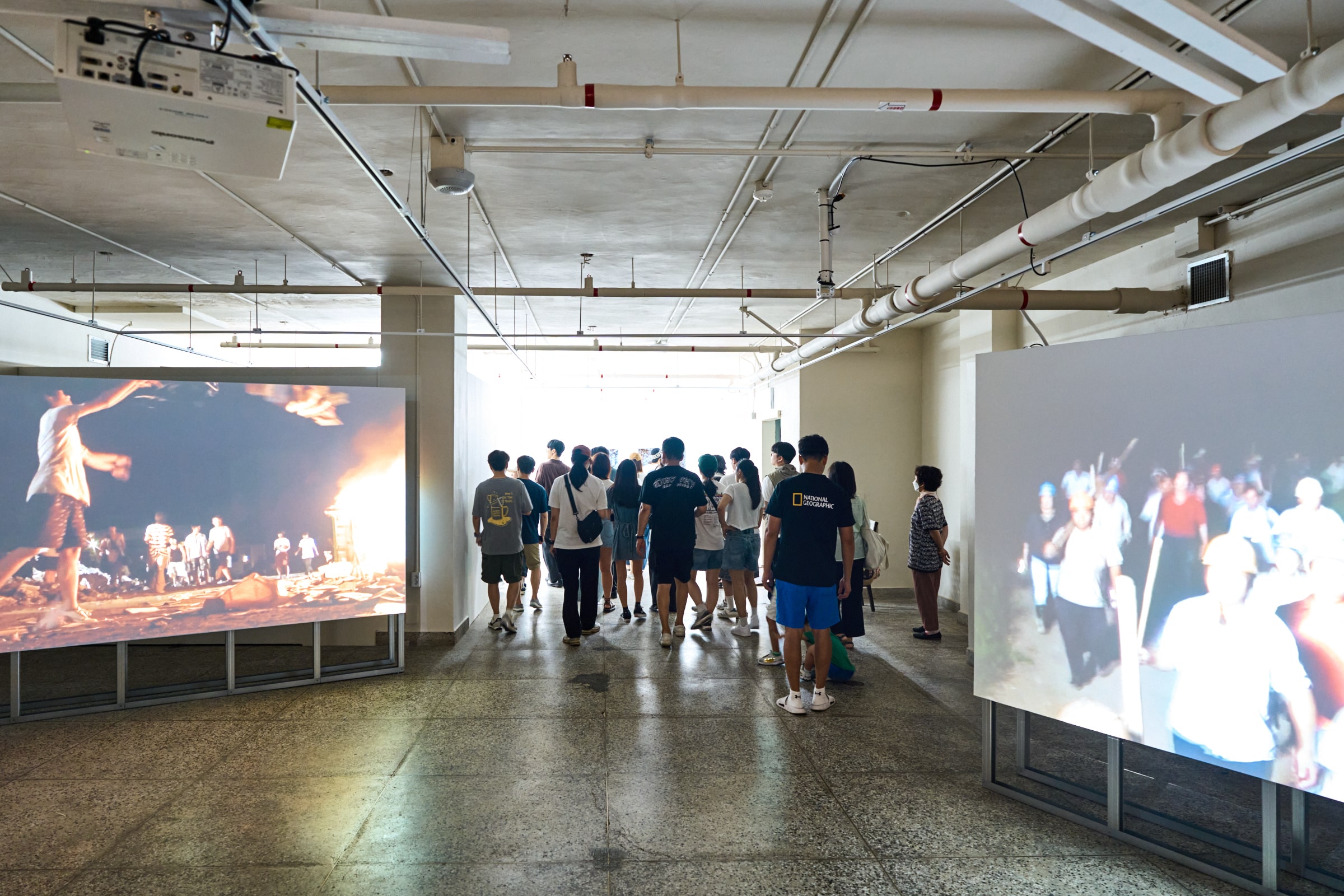 Installation shot of audience members amidst Chen Xiaoyun's Night/2.4KM (2009) and FIRE-3000KG (2009), single-channel video works.