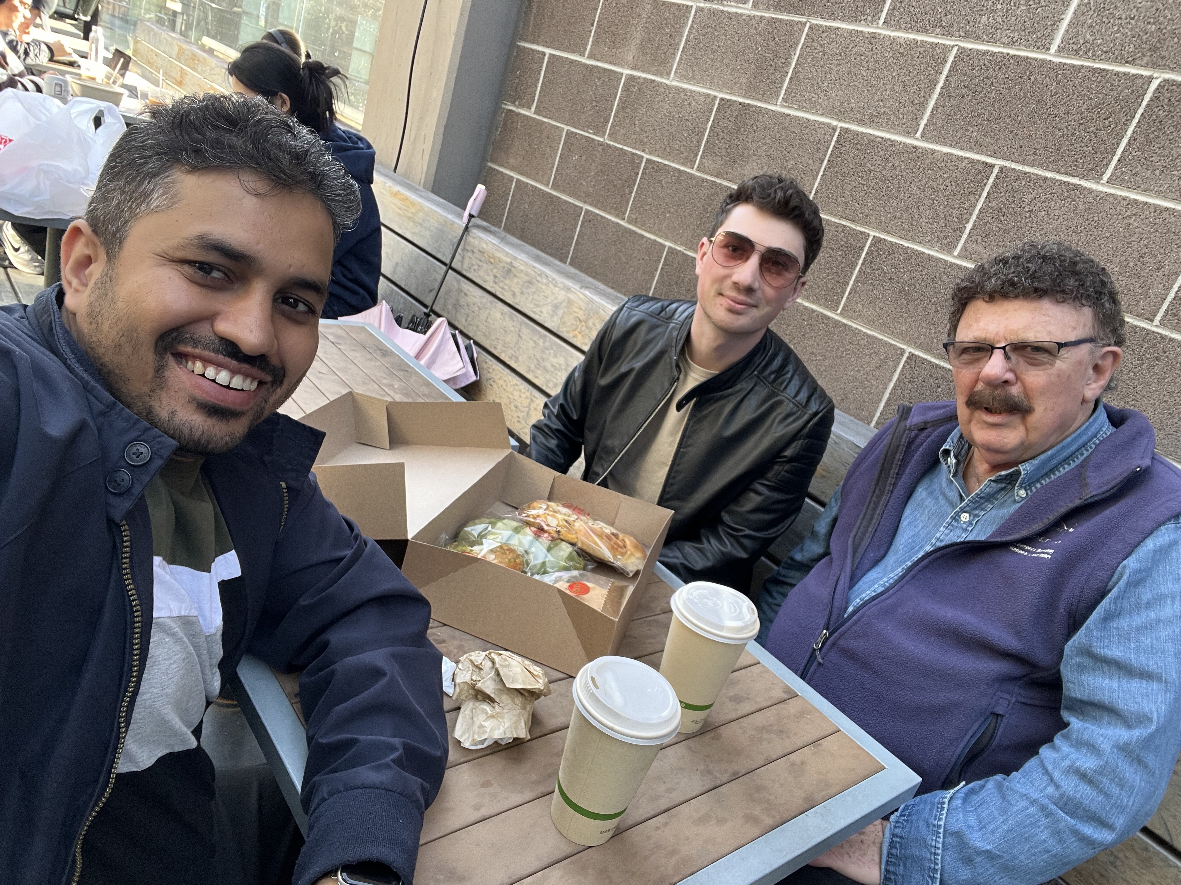 Asst Prof Punit Kumar, David Cook and Prof Robert Ritchie at a cafe table with coffee and pastries