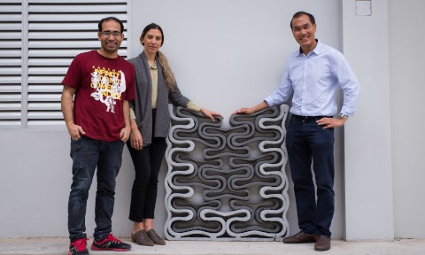 Prof and researchers pose next to a 3D printed wall made from geopolymer material