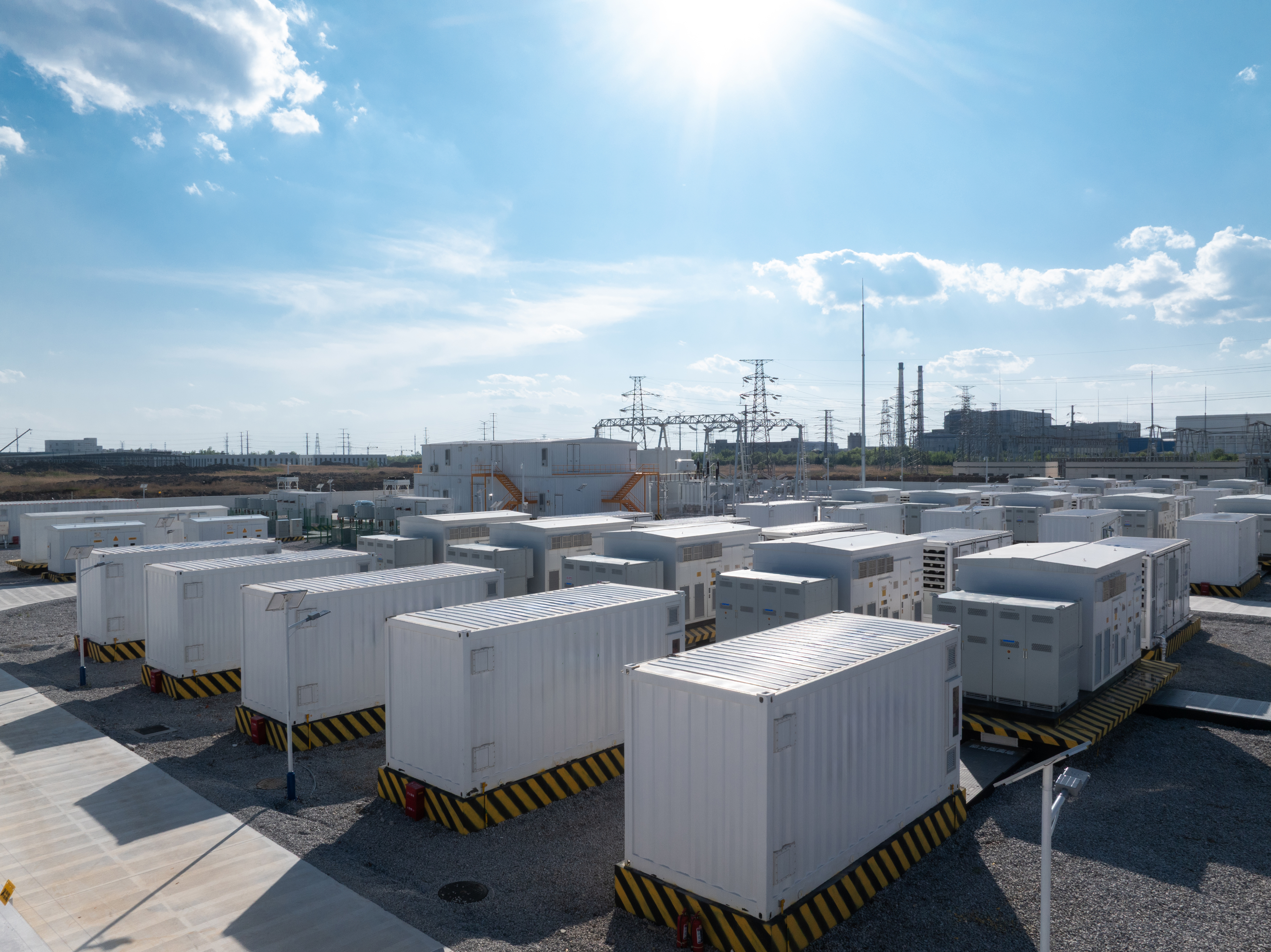 White containerised energy storage systems arranged in an outdoor power station facility