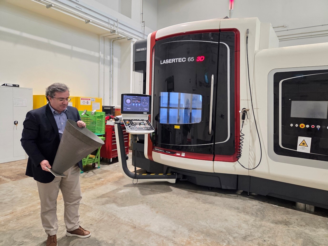 Bartolo holds a printed aircraft nozzle in front of the centre’s LaserTec 65 3D printing machine