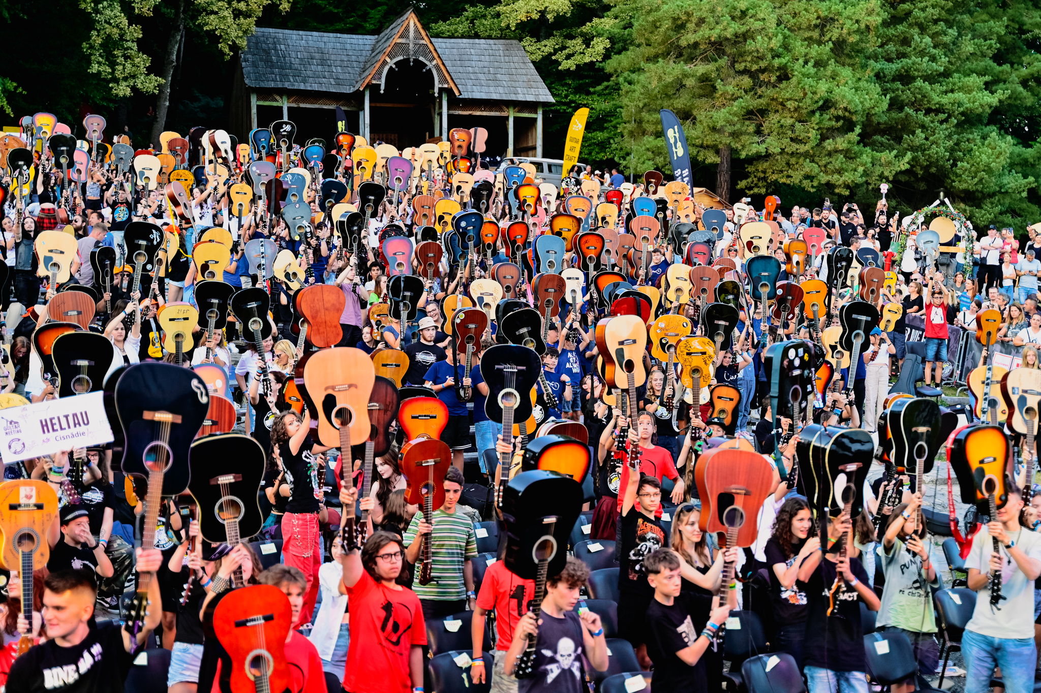 Hundreds of people outdoors hold colourful guitars above their heads in unison