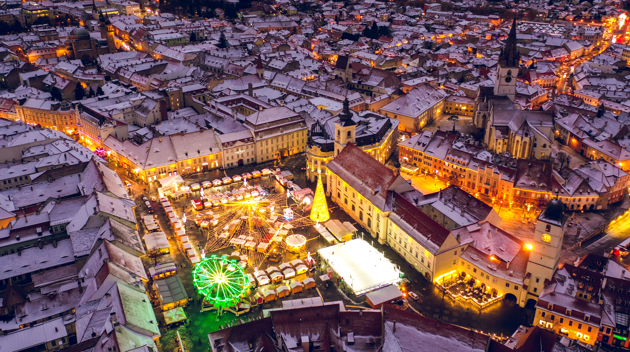 Aerial night view of a snow-covered old town square with a Christmas market, Ferris wheel and lit tree
