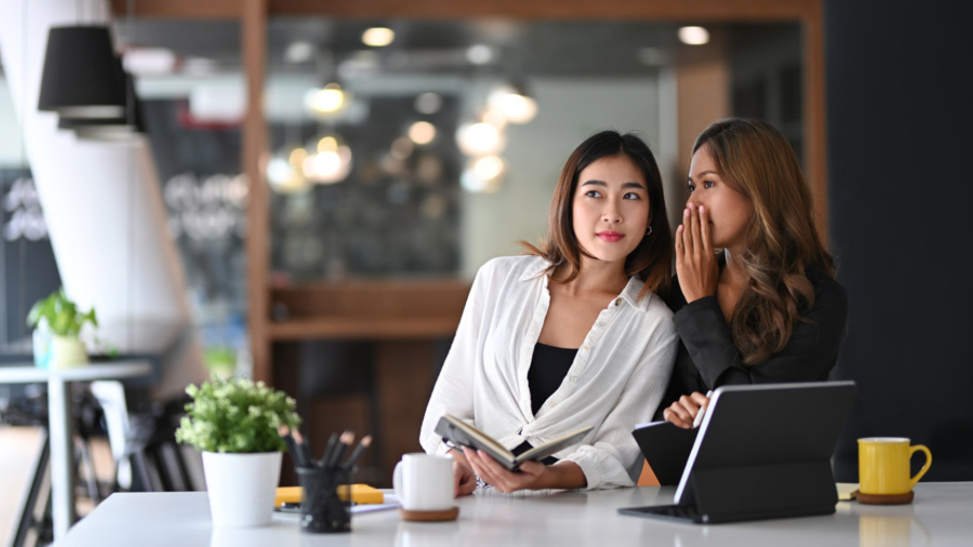 A woman whispering to a fellow female colleague