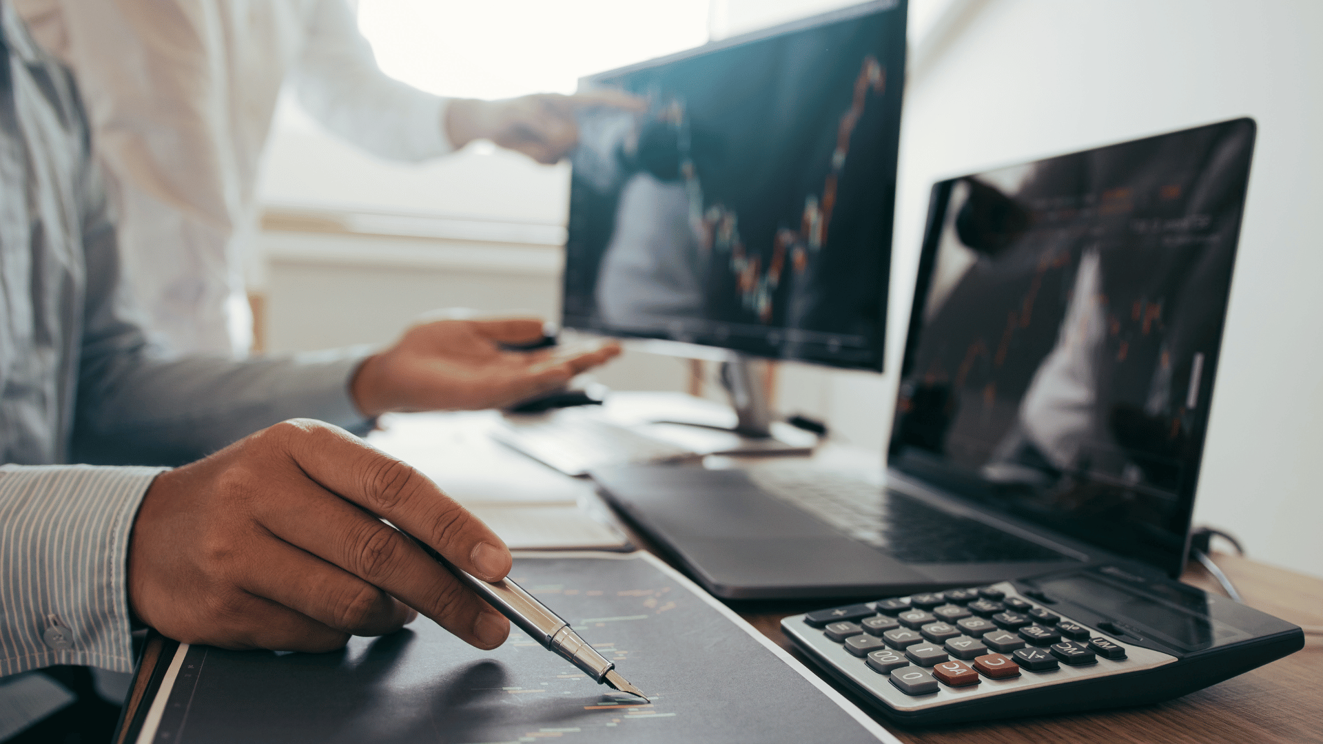 Investors analysing stock data graphs on paper and viewing data on laptop screen