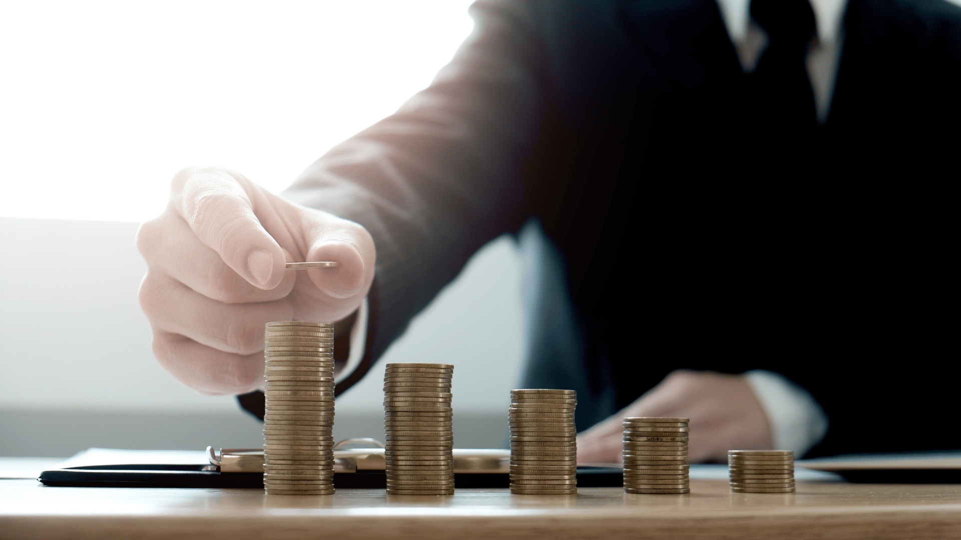 Coins stacked in ascending levels with a businessman placing a coin on a stack of coins Coins stacked in ascending levels with a businessman placing a coin on a stack of coins