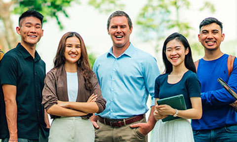 Smiling Group of 7 Young Adult Teachers Chinese Boy Yellow Gingham Plaid Shirt Caucasian Man Light Blue Shirt Super Closeup